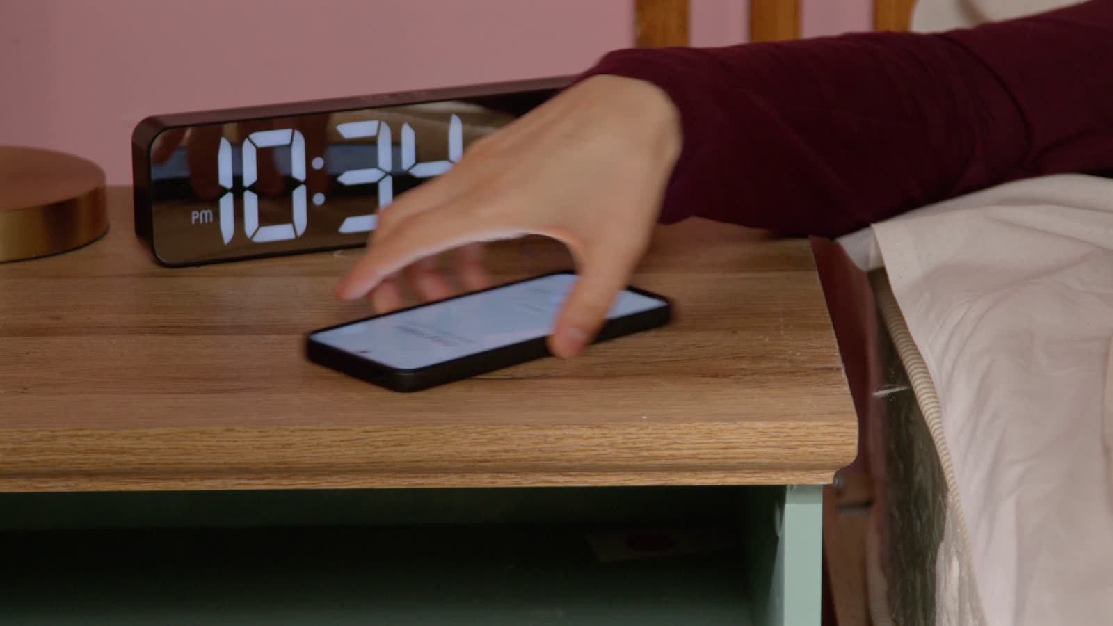A hand reaching for a phone on a nightstand